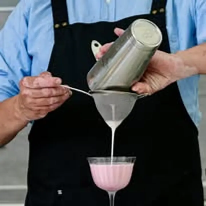 Bartender straining a pink cocktail into a coupe glass